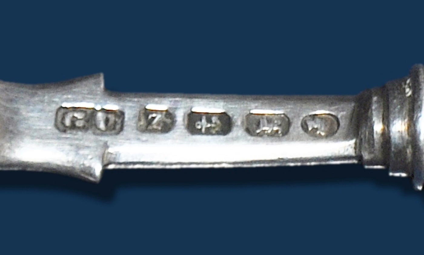 Stylised close-up of a Birmingham silver spoon hallmark showing anchor town mark, lion passant, date letter, maker's initials, and Victorian duty mark